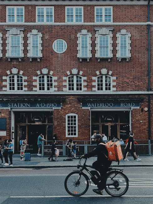 This image does not depict flowers, floral arrangements, or related materials and instead shows a street scene in front of Waterloo station. A man wearing a helmet and dark clothing is riding a bicycl